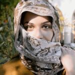 Close-up portrait of a woman wearing an ornate headscarf, showcasing her expressive eyes.